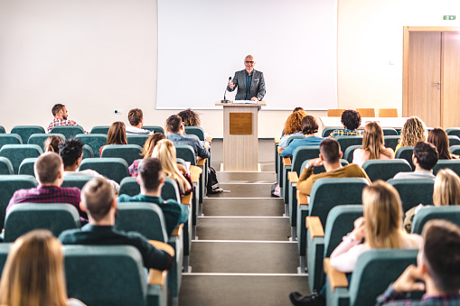 Happy senior teacher talking to large group of college students in amphitheater. Copy space.