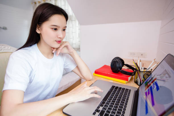 istock Asian woman, happy cheerful cute beautiful is using a notebook computer and sitting on a sofa for working from home. She is quarantined at home during the coronavirus epidemic. And she has sanitizer gel on the table for cleaning hands 1223138370
