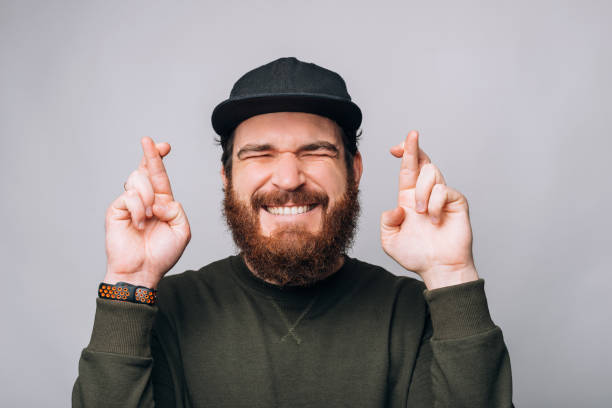 Young bearded man is wishing or hoping crossing fingers with eyes closed. stock photo