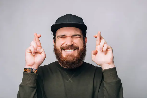 Photo of Young bearded man is wishing or hoping crossing fingers with eyes closed.