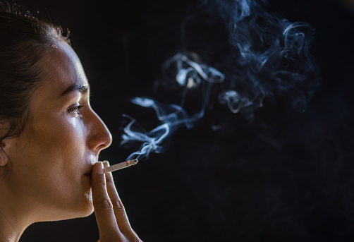Mid section of woman breaking cigarette against white background