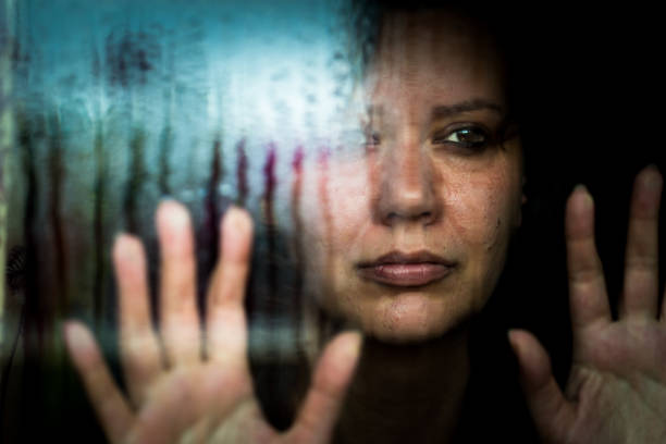 femme déprimé regardant par la fenêtre pluvieuse - pris au piège photos et images de collection