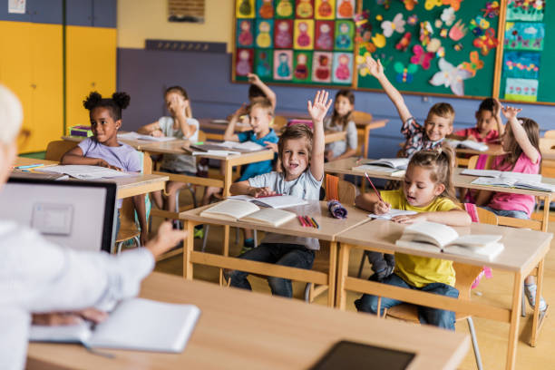 istock Happy elementary students raising hands to answer the teacher's question on a class. 1223141125