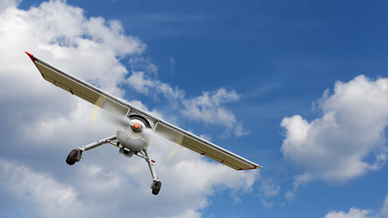 Light propeller-driven airplane flies against a background of cloudy blue sky. Copyspace.