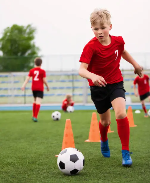 Soccer Boy on Training with Ball and Soccer Cones. Dribbling Drill. Soccer Kids Dribble Training. Youth Soccer Club Practice Session. Boys in Sports Team in Red Soccer Uniforms