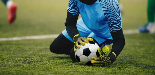 Photo of Soccer Football Goalkeeper Catching Ball. Goalie in Action on the Pitch During Match. Goalkeeper in a Goal Play in a Game