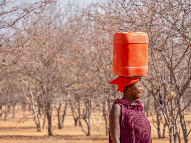 eine afrikanerin, die zurück in ihr ländliches dorf geht und eine kanister mit trinkwasser auf dem kopf trägt. - people effort waist up african ethnicity stock-fotos und bilder