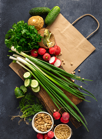 Food purchase concept. Paper bag with ingredients for cooking vegan eating. Fresh vegetables, herbs, cereal and nuts on dark background top view