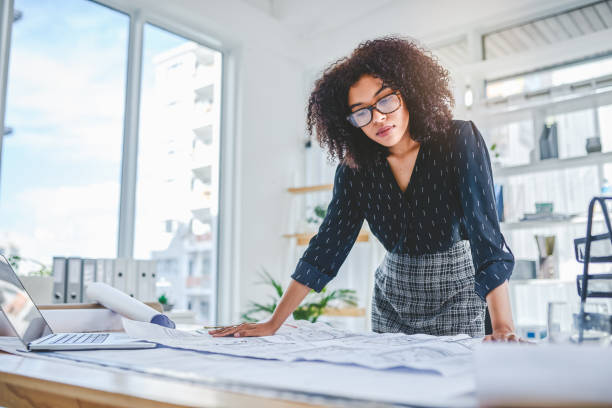Working on a few high-class designs Shot of a young businesswoman working with blueprints in an office african american architecture stock pictures, royalty-free photos & images