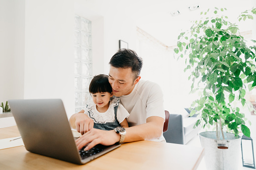 Padre e hija trabajando juntos en casa - La niña está siguiendo una lección de la escuela en línea photo