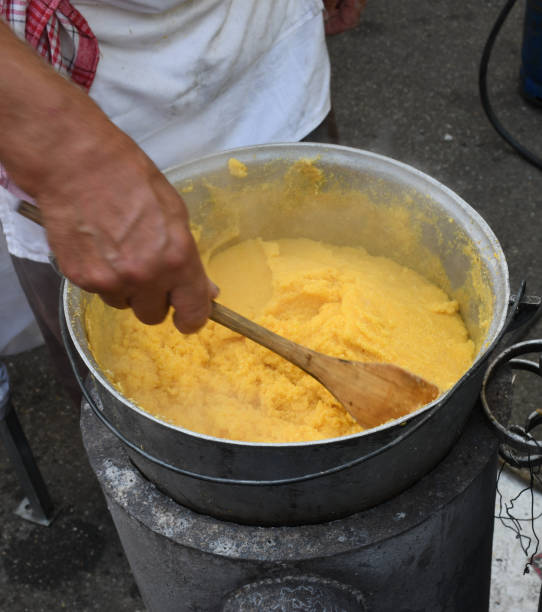 Fresh polenta or "mamaliga" cooking on large pot, chef stirring in pot over the fire Fresh polenta or "mamaliga" cooking on large pot, chef stirring in pot over the fire, during street food festival, agricultural event. Golden maize corn powder mixed with water,gluten free alternative mamaliga stock pictures, royalty-free photos & images