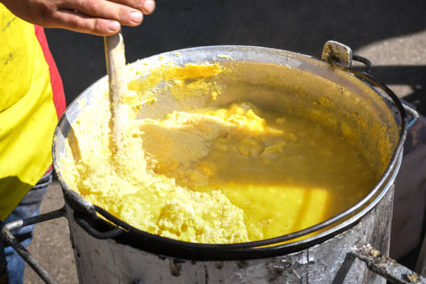 Fresh polenta or "mamaliga" cooking on large pot, chef stirring in pot over the fire Fresh polenta or "mamaliga" cooking on large pot, chef stirring in pot over the fire, during street food festival, agricultural event. Golden maize corn powder mixed with water,gluten free alternative mamaliga stock pictures, royalty-free photos & images