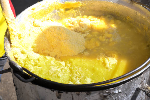 Fresh polenta or "mamaliga" cooking on large pot, chef stirring in pot over the fire Fresh polenta or "mamaliga" cooking on large pot, chef stirring in pot over the fire, during street food festival, agricultural event. Golden maize corn powder mixed with water,gluten free alternative mamaliga stock pictures, royalty-free photos & images