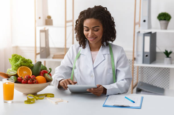 Dietologist black woman working with digital tablet at workplace Pretty dietologist black woman working with digital tablet at workplace nutritionist stock pictures, royalty-free photos & images