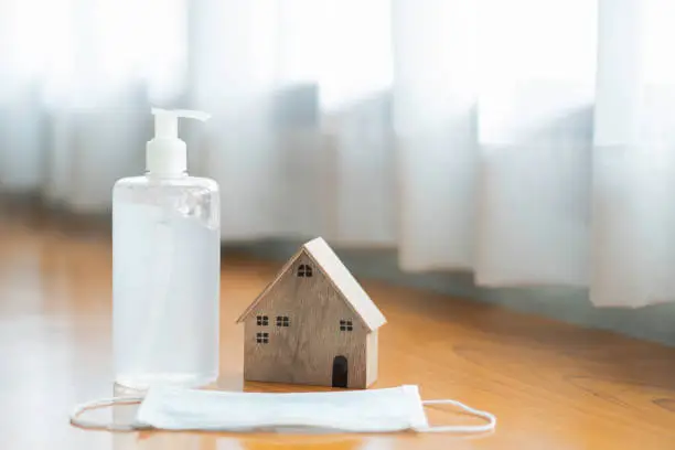 Photo of Alcohol hand gel sanitizer with medical protective mask and wooden house model. prevention supply during stay at home for self quarantine of Coronavirus or Covid-19 virus disease epidemic outbreak