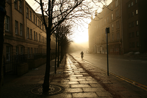 December 29, 2010 - Edinburgh, Scotland:  a cyclist on a bike cycling in an empty street in Edinburgh in winter fog with sun rising and shining brightly in the morning.