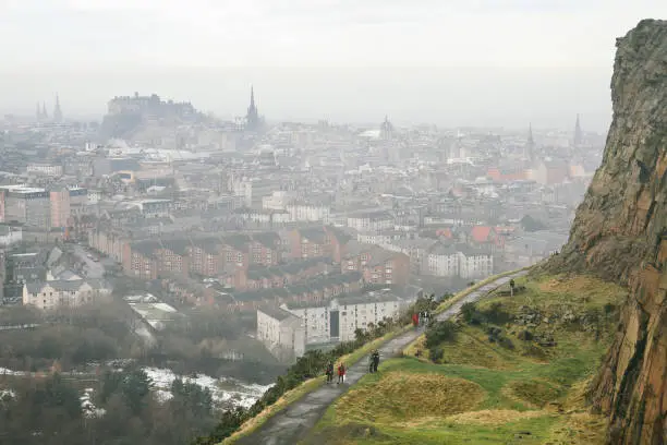 December 29, 2010 - Edinburgh, Scotland: hikers and tourists walking on a path to the Arthur's Seat mountain peak in winter in fog with Edinburgh panorama and skyline and Edinburgh Castle visible in the distance