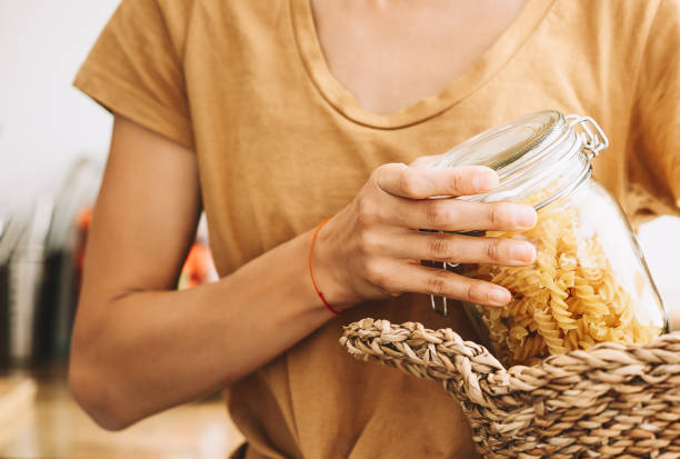 Woman buying products in plastic free grocery store. Glass jar with pasta in hands of person in zero waste shop. Woman buying products in plastic free grocery store. Glass jar with pasta in hands of person in zero waste shop. Young girl with wicker basket makes conscious shopping. Sustainable small businesses. local products stock pictures, royalty-free photos & images