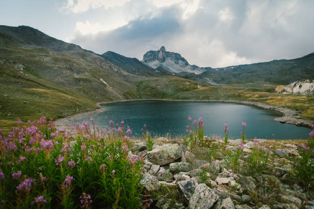 A wide landscape of a lake in the middle of the French Alpes surrounded by mountains stock photo