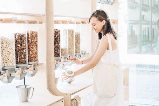 Woman with cotton bag and glass jar buying in zero waste shop. Dispensers for cereals, grains, nuts in plastic free grocery store. Woman with cotton bag and glass jar buying in zero waste shop. Dispensers for cereals, grains, nuts in plastic free grocery store. Sustainable shopping at small local businesses. Eco Bio Organic Food change dispenser stock pictures, royalty-free photos & images