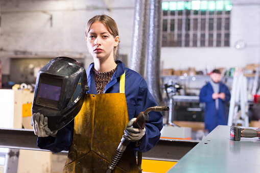 Young woman using welder for construction work at the workshop