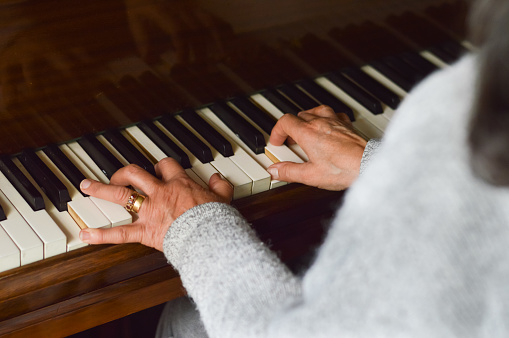 Over-the-shoulder shot of a pianist playing. Her hands are old and bear a wedding ring.