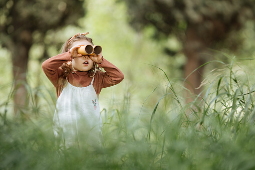 Child playing with binocular pretend safari game outdoors in the forest