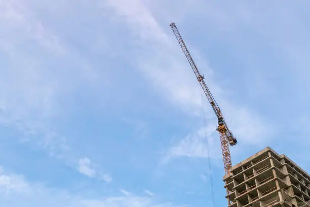 High rise building construction site with yellow crane against blue sky. Industrial background image with copy space for text.