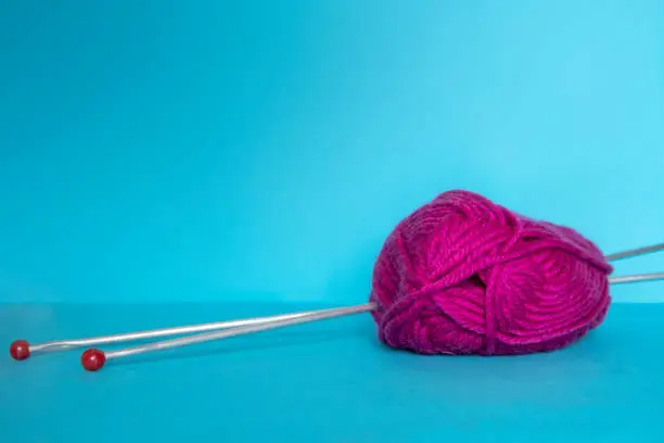 Woolen yarn pink for knitting and 2 metal needles on blue surface. Selective focus. Copy space for text.