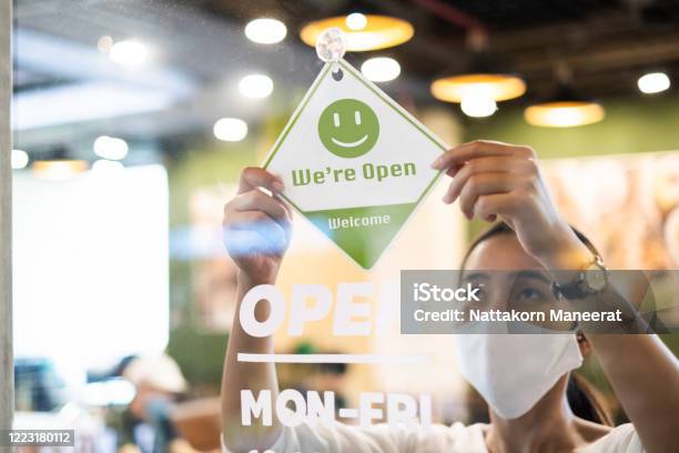 Business Owner Asian Woman Wear Protective Face Mask Ppe Hanging Open Sign At Her Restaurant Café Open Again After Lock Down Due To Outbreak Of Coronavirus Covid19 Stock Photo - Download Image Now