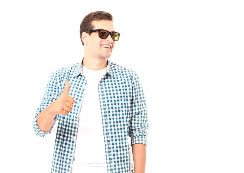Stylish smiling guy. Cheerful young handsome man in sunglasses with thumb up and looking away with smile isolated on white