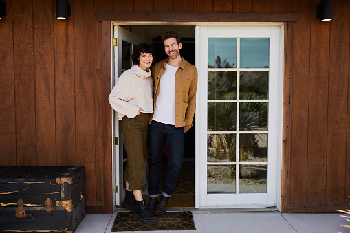 Portrait of a smiling young couple standing together at the front door of their home