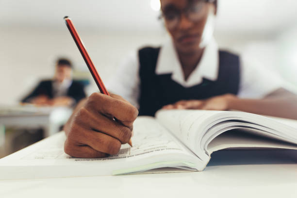 étudiant féminin écrivant dans le livre pendant la classe - book working college student classroom photos et images de collection