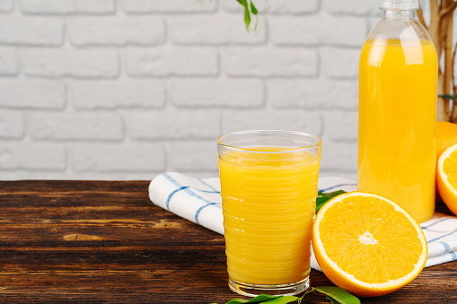 Bottle of fresh orange juice on wooden table against white brick wall background. Close up.