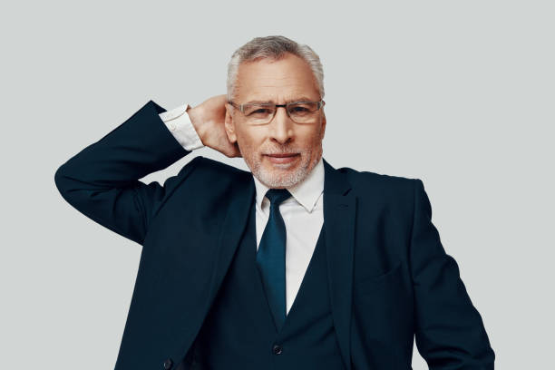 istock Handsome senior man in full suit looking at camera and smiling while standing against grey background 1223203742
