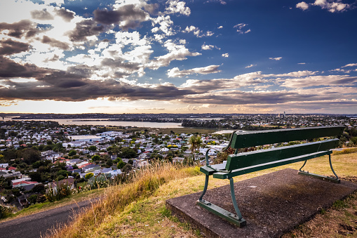 Bench on the hill over Auckland city skyline at sunset after heavy storm with city center and Auckland Sky Tower, the iconic landmark of Auckland, New Zealand.