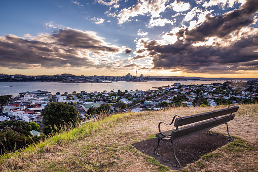 Bench on the hill over Auckland city skyline at sunset after heavy storm with city center and Auckland Sky Tower, the iconic landmark of Auckland, New Zealand.