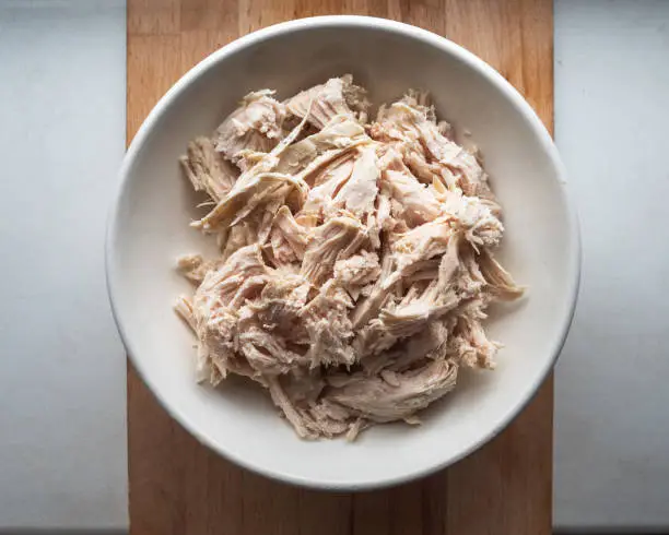 Chopped chicken meat for salads in a deep plate is on the kitchen board, top view