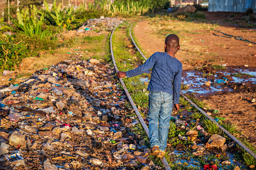 African little boy walking on railroad tracks, Kibera slum on the background, Kenya, East Africa. Kibera is the largest slum in Nairobi, the largest urban slum in Africa, and the third largest in the world