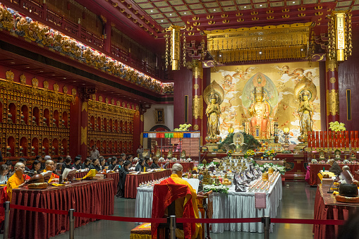 Singapore - December 01, 2018: Buddhist monks and believers chant mantras inside the Buddha Tooth Relic Temple in Singapore on December 01, 2018. The Buddha Tooth Relic Temple and Museum has been built in the architectural style of the Tang dynasty and is said to house a tooth relic of the historical Buddha. It is located in 228 South Bridge Road, Singapore.