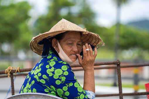 Danang, Vietnam - april 26, 2020 : Vietnamese woman in a straw hat with a cigarette in hand on a street market in the city of Danang, Vietnam. Close up