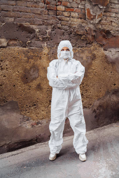 istock People's lives depend on doctors! Confident doctor, dressed in a white protective suit and protective mask, folded her arms over her chest. Stands on the street against scratched wall. Covid-19 1223218730