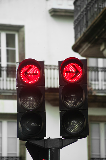 Red traffic lights, arrow symbols pointing in opposite direction. Traditional building facades background.