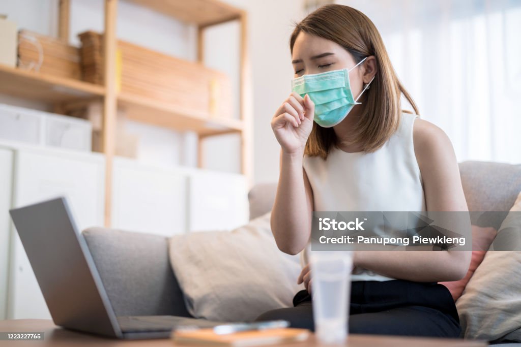 Young Asian woman wearing mask is work at home, She coughed and sore throat. Coughing Stock Photo