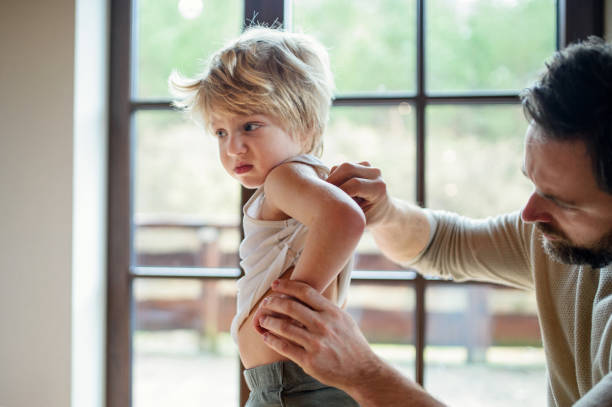 Father with small sick unhappy son indoors at home, checking his back. Father with small sick unhappy son indoors at home, checking his hurt back. skin condition photos stock pictures, royalty-free photos & images