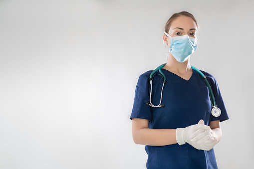Portrait of a female doctor with face mask standing confidently  on a white background