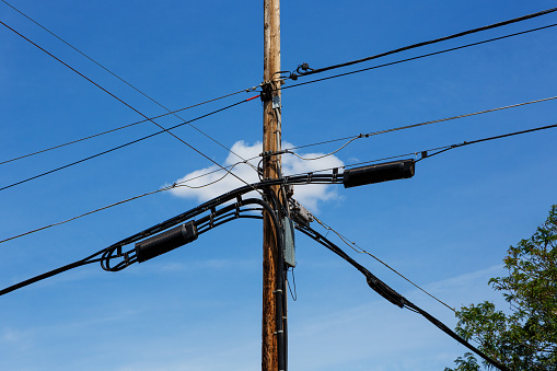 Telephone and Power pole with utility wires intersecting with a single white cloud behind it against a blue sky