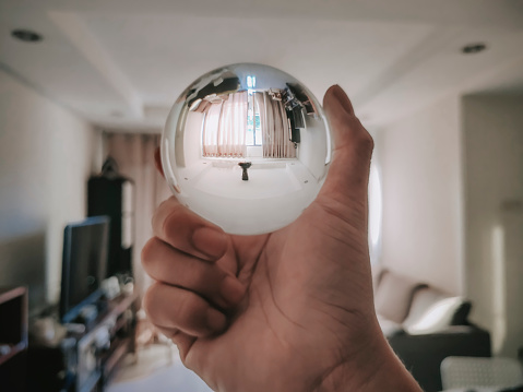 reflection of crystal ball with human hand holding it on living room during sunset