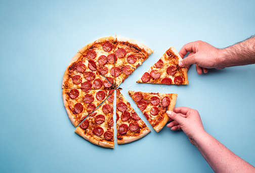 Man and woman hands grabbing pizza slices. Sliced pepperoni pizza on a blue background, above view. Top view with delicious pepperoni pizza.
