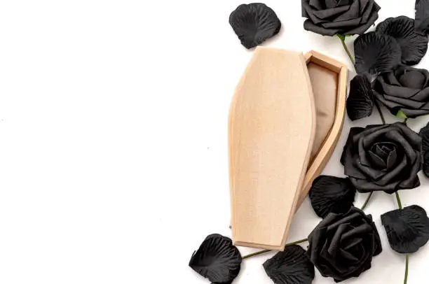 Photo of Last goodbye, grief for the deceased and sadness of losing loved ones concept with wood coffin surrounded by black roses isolated on white background with copy space